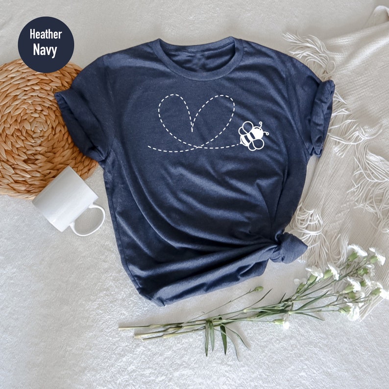 Peut inclure: Un t-shirt bleu marine chin&eacute; avec une abeille blanche volant en ligne pointill&eacute;e qui forme un c&oelig;ur.