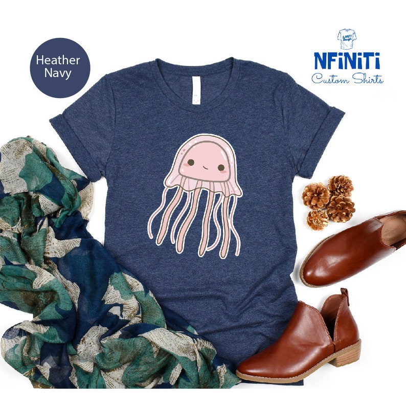 May include: Heather navy blue t-shirt with a cute cartoon jellyfish graphic. The jellyfish is pink with a white face and has long pink tentacles. The shirt has a crew neck and short sleeves. The text "NFINITI Custom Shirts" is in the top right corner of the image.