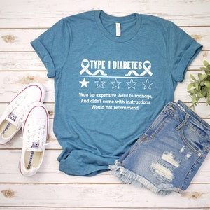 K&ouml;nnte beinhalten: Ein t&uuml;rkisfarbenes T-Shirt mit einer wei&szlig;en Grafik, auf der "TYPE 1 DIABETES" mit einem Band und vier Sternen steht. Der Text unter der Grafik lautet "Way to expensive, hard to manage, And didn't come with instructions Would not recommend."
