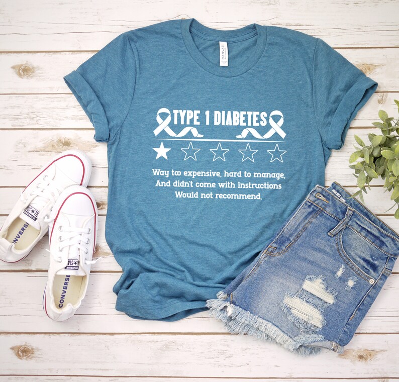 K&ouml;nnte beinhalten: Ein t&uuml;rkisfarbenes T-Shirt mit einer wei&szlig;en Grafik, auf der "TYPE 1 DIABETES" mit einem Band und vier Sternen steht. Der Text unter der Grafik lautet "Way to expensive, hard to manage, And didn't come with instructions Would not recommend."
