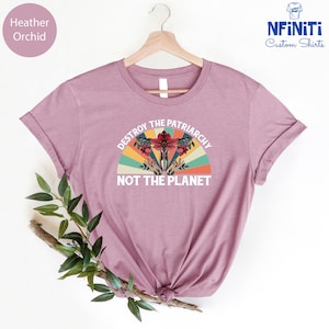 May include: A heather orchid t-shirt with a vintage-style graphic that says "Destroy the Patriarchy Not the Planet". The graphic features a stylized uterus with flowers and a rainbow.