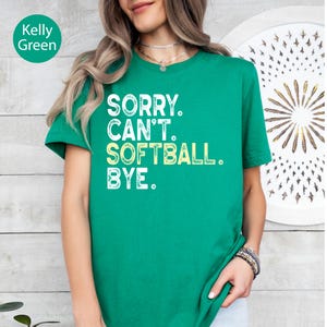 May include: A Kelly green short-sleeved t-shirt featuring the white and light yellow distressed text that reads: SORRY. CAN'T. SOFTBALL. BYE. The shirt has a crew neckline and a standard fit, showcasing a bold graphic print on the front.