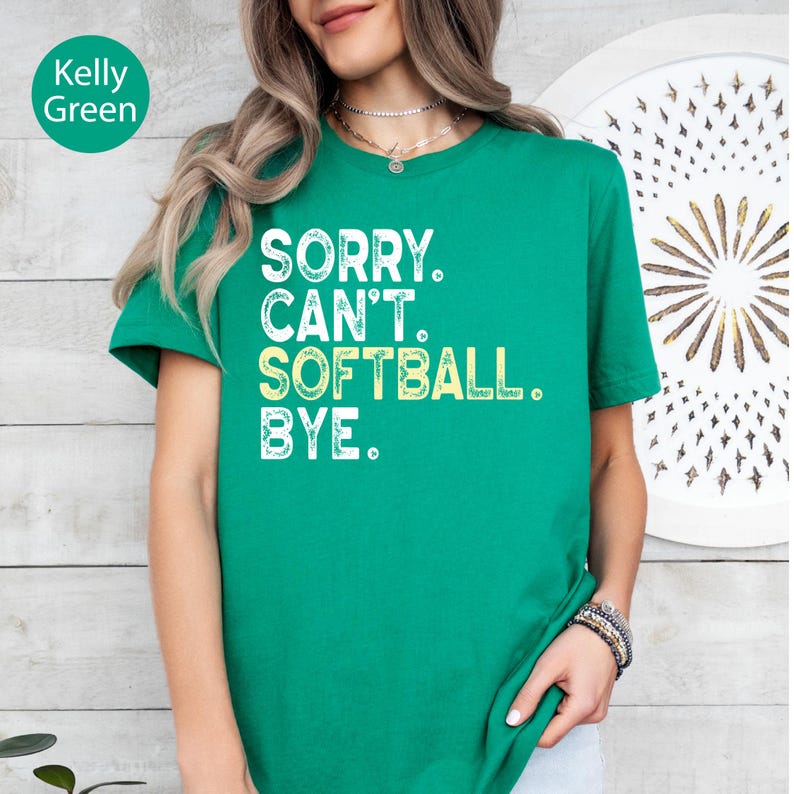 May include: A Kelly green short-sleeved t-shirt featuring the white and light yellow distressed text that reads: SORRY. CAN'T. SOFTBALL. BYE. The shirt has a crew neckline and a standard fit, showcasing a bold graphic print on the front.