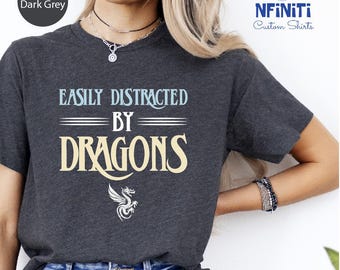 May include: A heather dark grey t-shirt with the text "Easily Distracted By Dragons" in white and yellow lettering. A small white dragon graphic is below the text.