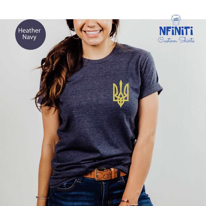 May include: A heather navy blue t-shirt with a yellow embroidered Ukrainian trident symbol. The t-shirt is made by NFINITI Custom Shirts.