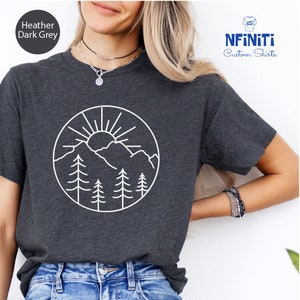 a woman wearing a t - shirt with a picture of mountains and trees on it