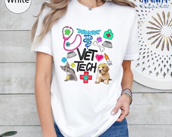May include: White t-shirt with a colorful "Vet Tech" design. The design includes a stethoscope, medical symbols, paw prints, and illustrations of a cat and a puppy. The shirt is a crew neck style.