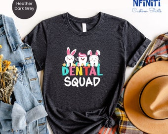 May include: A heather dark grey t-shirt with a graphic of three cartoon teeth wearing bunny ears and holding Easter eggs. The text "Dental Squad" is printed below the teeth.