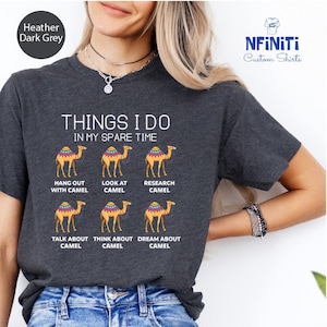 May include: A dark heather grey t-shirt with the text "THINGS I DO IN MY SPARE TIME" and six illustrations of camels. The text below each camel reads "HANG OUT WITH CAMEL", "LOOK AT CAMEL", "RESEARCH CAMEL", "TALK ABOUT CAMEL", "THINK ABOUT CAMEL", and "DREAM ABOUT CAMEL".