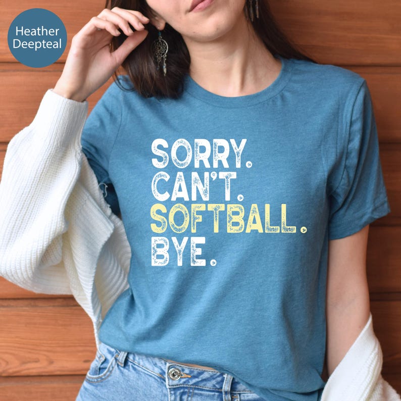 May include: A teal t-shirt with the text "SORRY. CAN'T. SOFTBALL. BYE." in white and yellow lettering. The shirt is short-sleeved and made of a soft material. The words are stacked vertically.