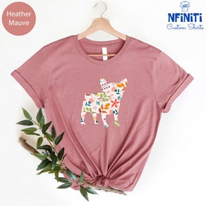 Peut inclure: Un t-shirt en mauve chin&eacute; avec un imprim&eacute; floral en forme de silhouette de bouledogue fran&ccedil;ais. Le t-shirt est sur un cintre et a un fond blanc.