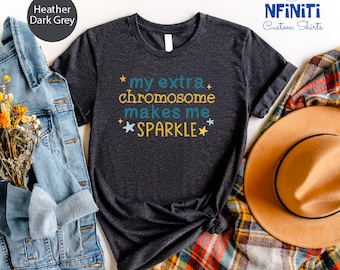 Può includere: Una maglietta grigia scura melange con il testo "*my extra chromosome makes me SPARKLE*" stampato sul davanti. Il testo è in blu e giallo con stelle su entrambi i lati.
