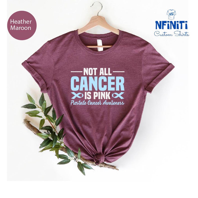 May include: Heather maroon t-shirt with the text "Not all cancer is pink" and a blue ribbon symbol. The text "Prostate Cancer Awareness" is below the ribbon.