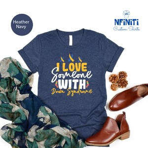 May include: A navy blue t-shirt with the text "I love someone with Down Syndrome" in yellow and blue. Three yellow ribbons are above the text.