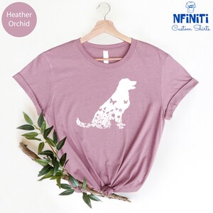 May include: A heather orchid t-shirt with a white silhouette of a dog made up of flowers and butterflies. The text "NFINITI Custom Shirts" is in the top right corner of the image.