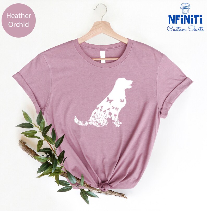 May include: A heather orchid t-shirt with a white silhouette of a dog made up of flowers and butterflies. The text "NFINITI Custom Shirts" is in the top right corner of the image.