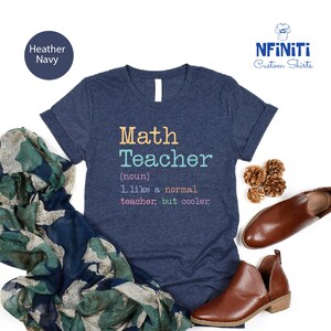May include: Heather navy t-shirt with the text "Math Teacher" in colorful letters. The definition below reads "1. like a normal teacher, but cooler." The shirt is paired with brown leather shoes and a patterned scarf.