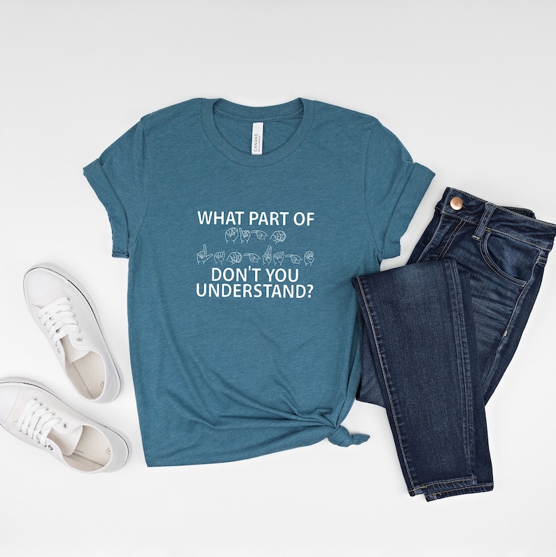 May include: A teal blue t-shirt with the text "WHAT PART OF DON'T YOU UNDERSTAND?" in white. The text is accompanied by a row of hand signs in American Sign Language.