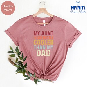 May include: Heather mauve t-shirt with the text "My Aunt is Definitely Cooler Than My Dad" in a retro font with colorful accents.