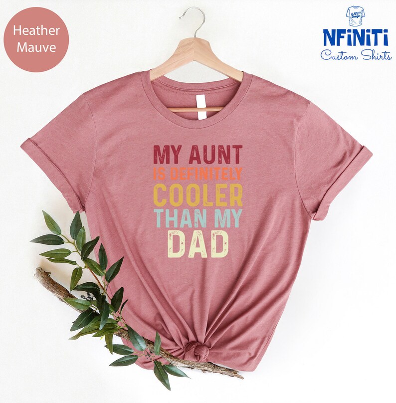 May include: Heather mauve t-shirt with the text "My Aunt is Definitely Cooler Than My Dad" in a retro font with colorful accents.