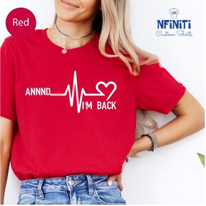 Op de afbeelding: Rood T-shirt met een witte hartslaggrafiek en de tekst "ANNNND I'M BACK" met een hart aan het einde.