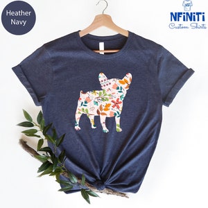 Peut inclure: Un t-shirt bleu marine chin&eacute; avec un motif floral &agrave; l'int&eacute;rieur de la silhouette d'un bouledogue fran&ccedil;ais. Le t-shirt est sur un cintre.
