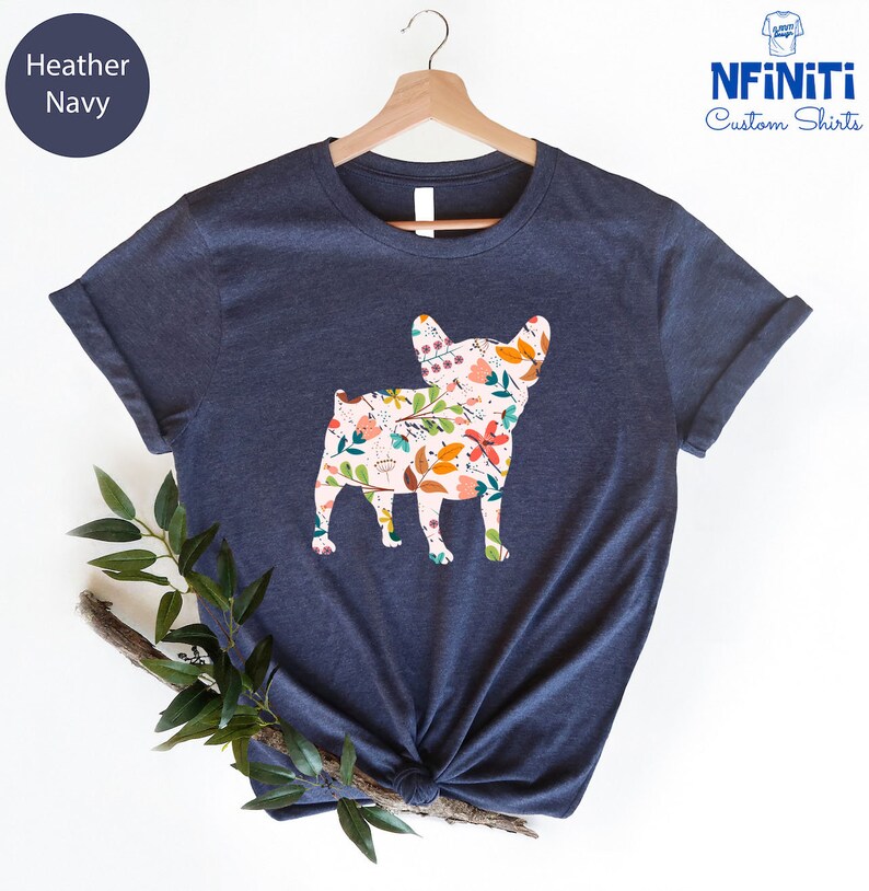 Peut inclure: Un t-shirt bleu marine chin&eacute; avec un motif floral &agrave; l'int&eacute;rieur de la silhouette d'un bouledogue fran&ccedil;ais. Le t-shirt est sur un cintre.
