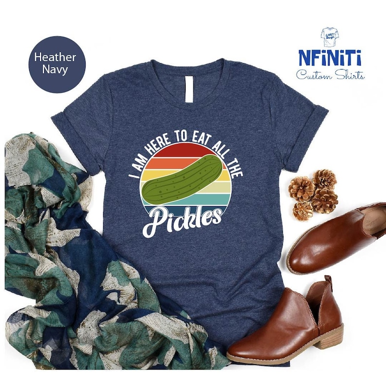 May include: A navy blue t-shirt with a vintage-style graphic of a pickle. The graphic says "I am here to eat all the pickles".