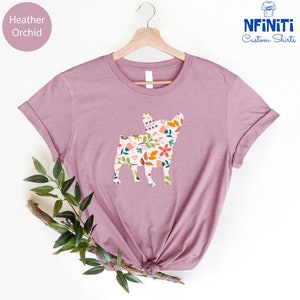 Peut inclure: Un t-shirt en heather orchid avec une silhouette de bouledogue fran&ccedil;ais &agrave; motif floral. Le t-shirt est sur un cintre et a un fond blanc.