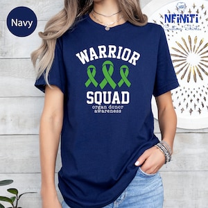 May include: Navy blue t-shirt with white text that reads "Warrior Squad organ donor awareness". Three green ribbon symbols are above the text.