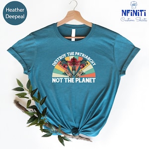 May include: Teal blue t-shirt with a vintage-style graphic of a uterus with flowers and the text "Destroy the Patriarchy Not the Planet."
