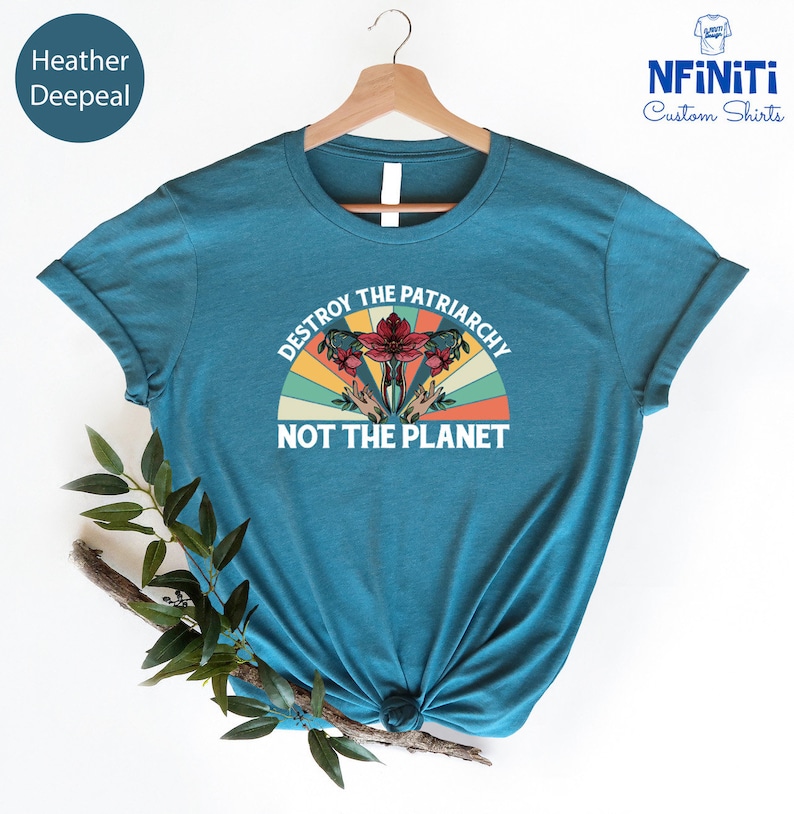 May include: Teal blue t-shirt with a vintage-style graphic of a uterus with flowers and the text "Destroy the Patriarchy Not the Planet."
