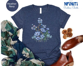 May include: Heather navy blue t-shirt with a floral design featuring blue flowers and green leaves. The shirt is displayed on a white background with a scarf and brown boots.