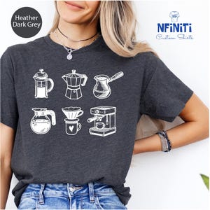 May include: Heather dark grey t-shirt featuring white line drawings of various coffee brewing devices. The shirt includes a French press, a stovetop espresso maker, a Turkish coffee pot, a glass carafe, a pour-over setup, and an espresso machine.