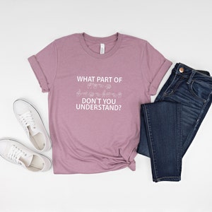 May include: A mauve t-shirt with the text "WHAT PART OF DON'T YOU UNDERSTAND?" in white lettering. The text is accompanied by a row of hand signs in American Sign Language.