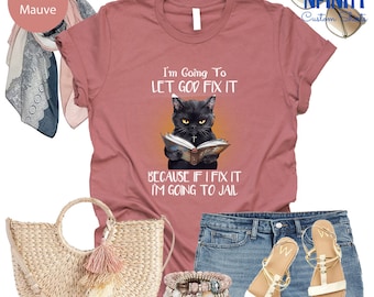 May include: A heather mauve t-shirt with a black cat reading a book. The text on the shirt reads "I'm Going To LET GOD FIX IT BECAUSE IF I FIX IT I'M GOING TO JAIL".