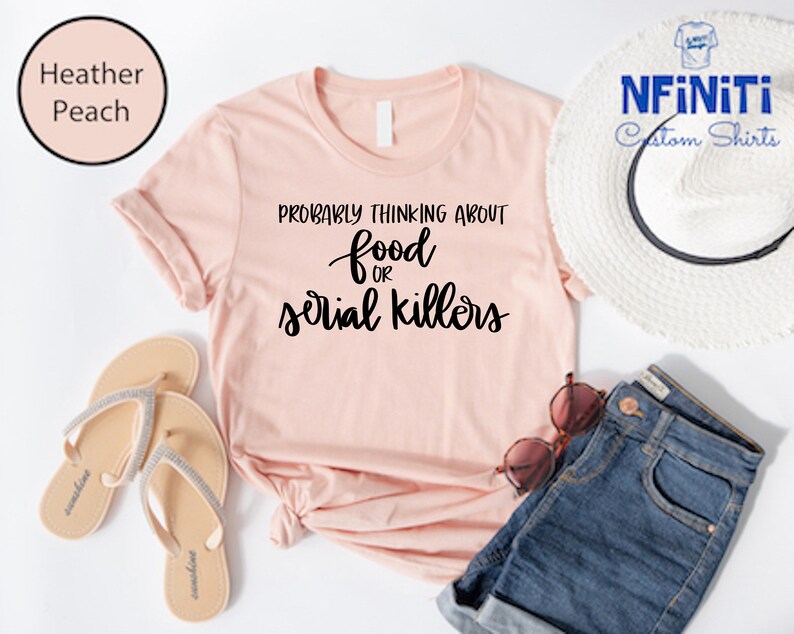 May include: A heather peach t-shirt with the text "Probably thinking about food or serial killers" in black.