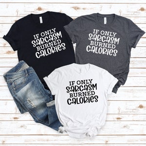 May include: Three t-shirts with the text "If only sarcasm burned calories" in black lettering on a white, dark grey, and black background.