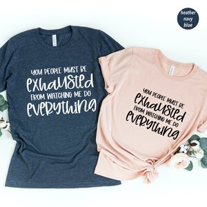 May include: Two t-shirts with the text "You people must be exhausted from watching me do everything" in black lettering on a heather navy blue and heather peach shirt.
