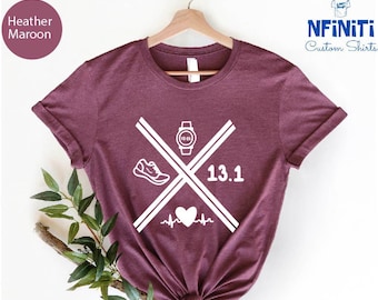 Könnte beinhalten: Heather-marronfarbenes T-Shirt mit einem weißen Grafikdesign, das einen Laufschuh, eine Uhr, ein Herz mit einer Herzschlaglinie und die Zahl 13.1 zeigt.