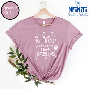 May include: A heather orchid t-shirt with a white graphic that says "I'm a math teacher of course I have problems" with math symbols and equations.