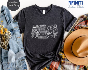 May include: A dark heather grey t-shirt with a white graphic of a typewriter, books, pencils, and other writing tools. The text "NFINTI Custom Shirts" is in the top right corner of the image.