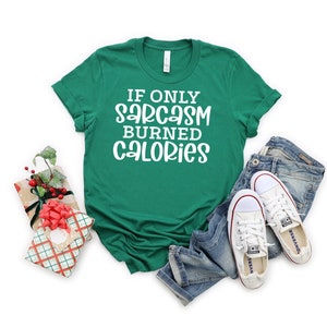 May include: A green t-shirt with white text that reads "If only sarcasm burned calories". The shirt is lying on a white background with a pair of blue jeans and white trainers.