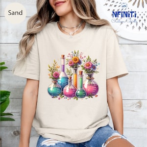 Può includere: Una maglietta bianca con una grafica di becher colorati con fiori al loro interno. Il testo "Infiniti Custom Shirts" è nell'angolo in alto a destra dell'immagine.