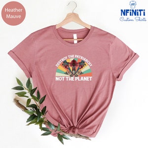 May include: Heather mauve t-shirt with a vintage-style graphic that says "Destroy the Patriarchy Not the Planet". The graphic features a stylized uterus with flowers and a rainbow.
