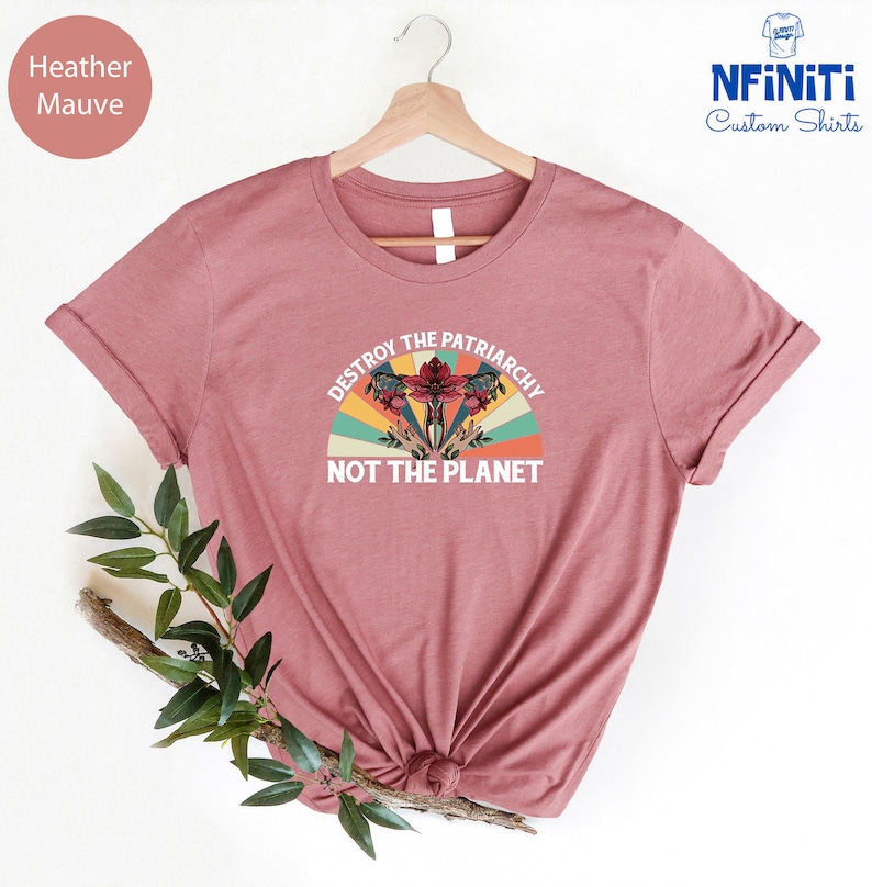 May include: Heather mauve t-shirt with a vintage-style graphic that says "Destroy the Patriarchy Not the Planet". The graphic features a stylized uterus with flowers and a rainbow.