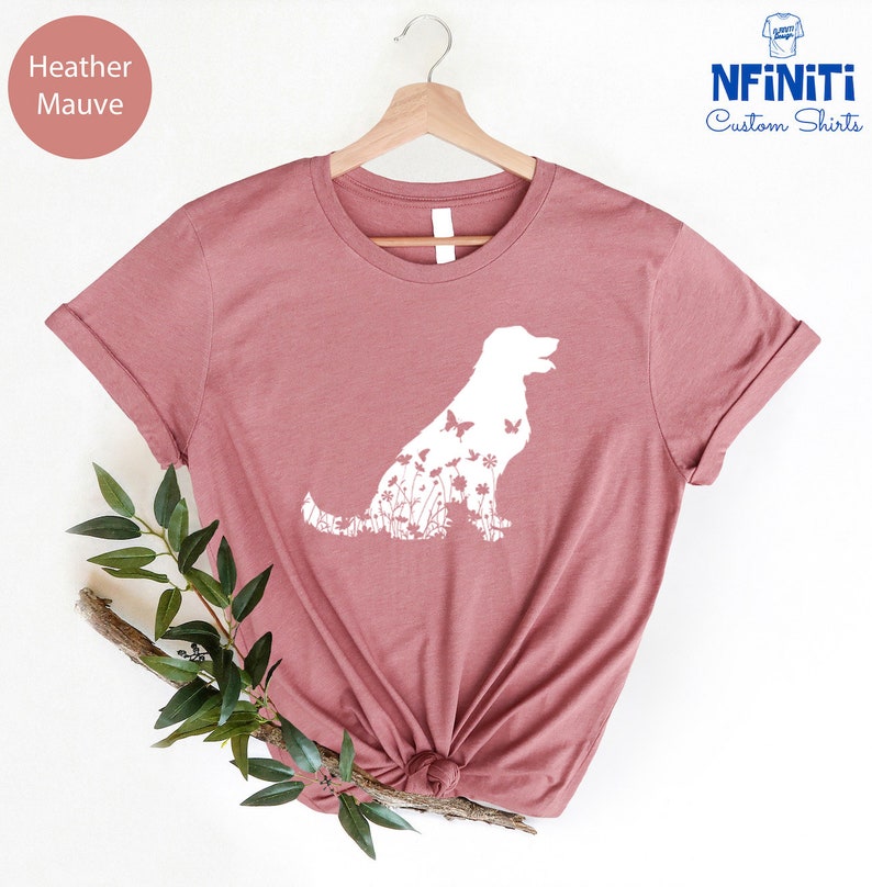 May include: Heather mauve t-shirt with a white silhouette of a dog with flowers and butterflies inside the silhouette. The shirt is on a hanger and has a white background.