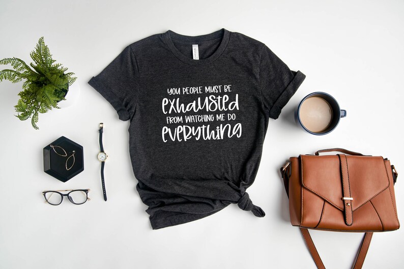 May include: A dark gray t-shirt with the text "You people must be exhausted from watching me do everything" in white lettering.