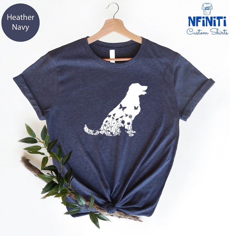 May include: A heather navy blue t-shirt with a white silhouette of a dog with flowers and butterflies inside the outline. The shirt is on a hanger.