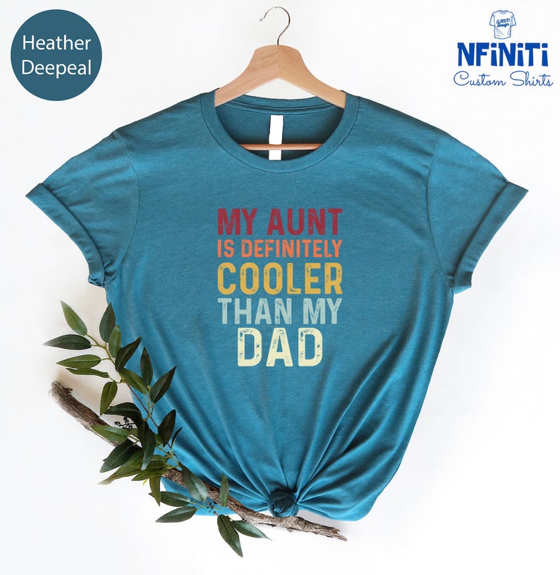 May include: Teal blue t-shirt with the text "My Aunt is Definitely Cooler Than My Dad" in a vintage style font with red, orange, and yellow colors.